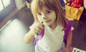 Little girl draws on her face with a marker