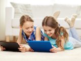 people, children, technology, friends and friendship concept - happy little girls with tablet pc computers lying on floor at home