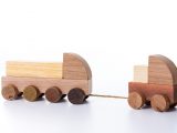 Small toy truck pulling another larger toy truck by a rope, both made of wood, with blocks to assemble.