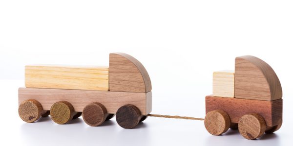 Small toy truck pulling another larger toy truck by a rope, both made of wood, with blocks to assemble.