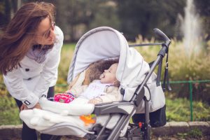 Mother with her baby in a stroller spending time together at the park,making faces