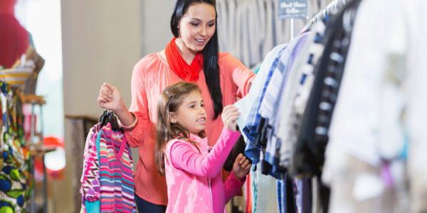 A young woman with her 7 year old daughter shopping in a clothing store. They are looking at a clothes rack.