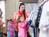 A young woman with her 7 year old daughter shopping in a clothing store. They are looking at a clothes rack.